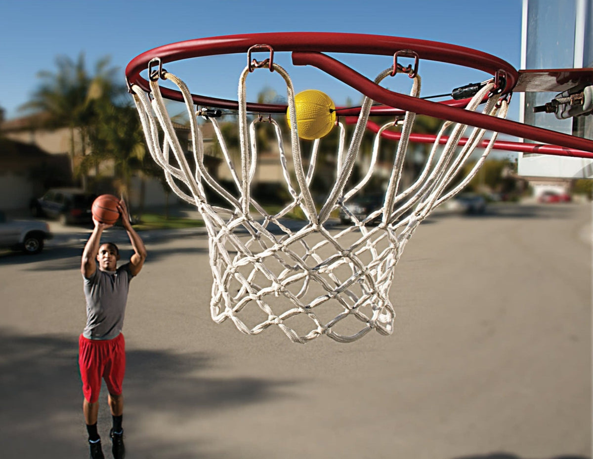 Player shooting a basketball on a driveway toward a hoop with a white nylon net and the yellow SKLZ shooting target clipped to the rim